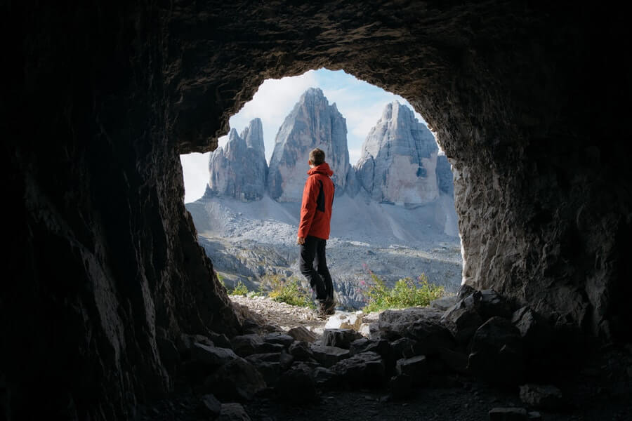 Man Outside cave in Front of 3 Mountains