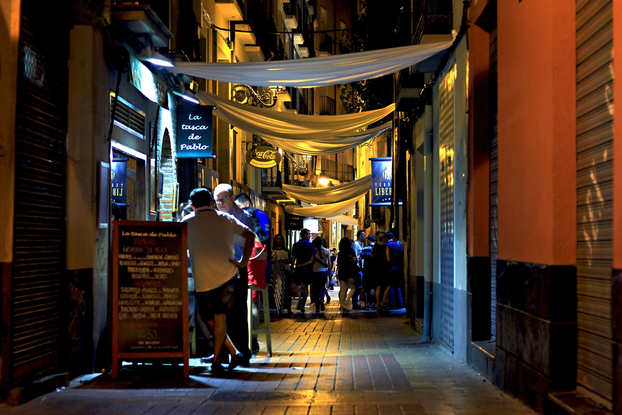 Lively city alley at night with people gathering in a bustling, illuminated nightlife district.