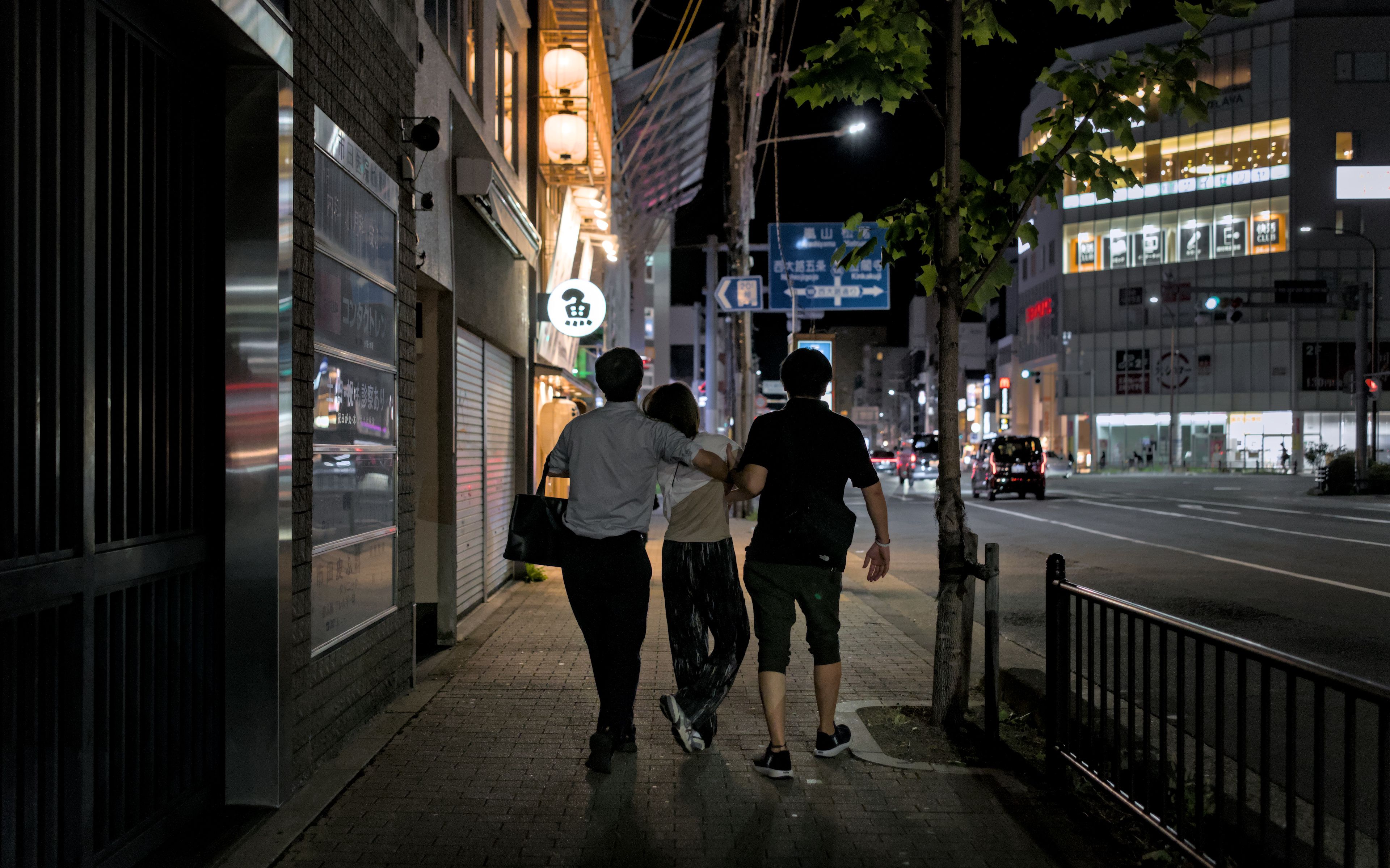 A group of friends enjoying a nighttime stroll through lively city streets in Kyoto.