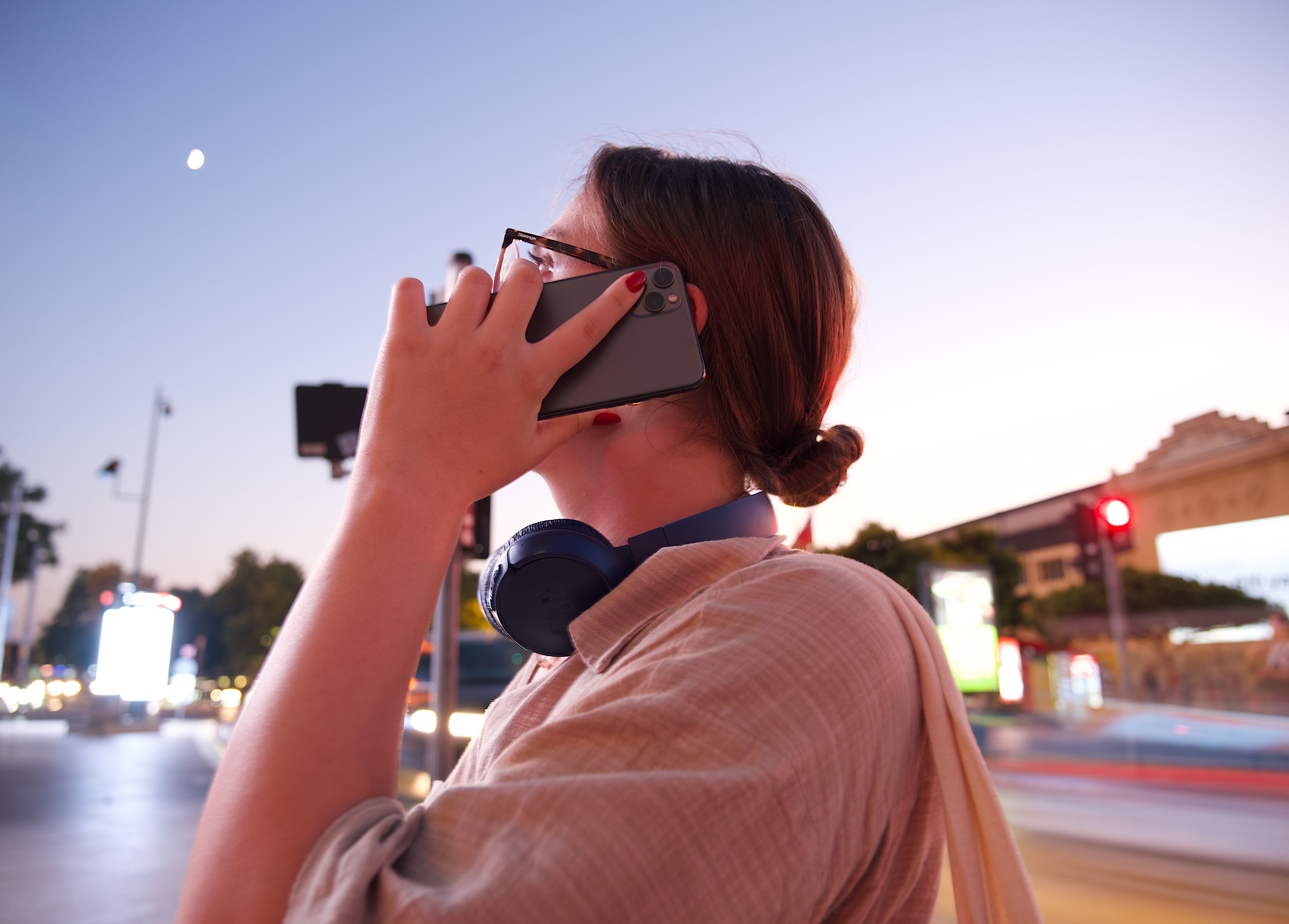 Woman talking on a smartphone at dusk with blurred urban lights behind her.